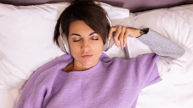 An image of a woman in bed with headphones on