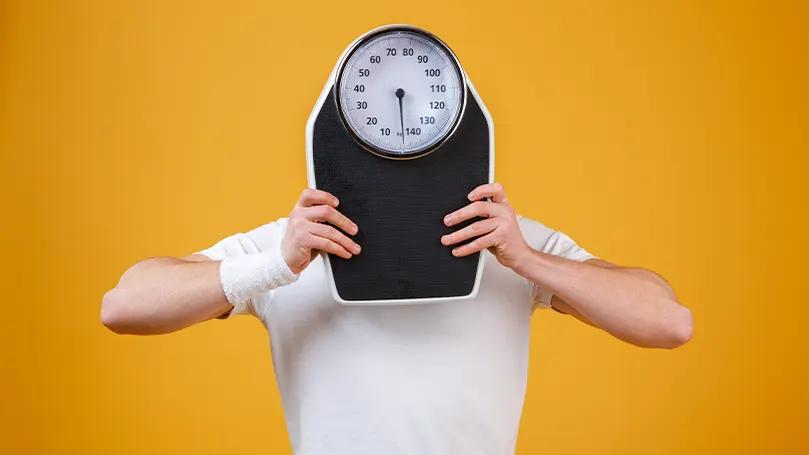 An image of a person holding a scale in front of their face