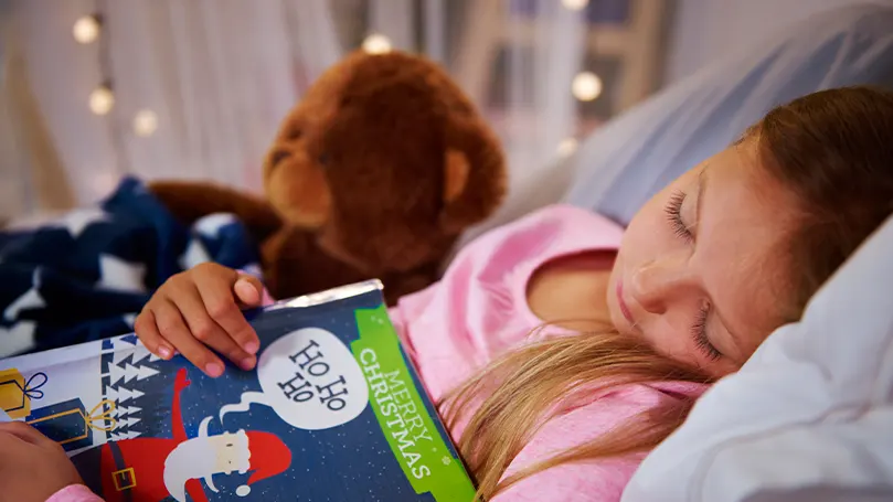 An image of a child sleeping and holding a book.