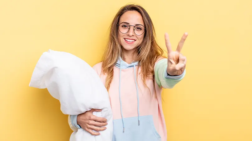 An image of a woman holding a body pillow and holding up a peace sign