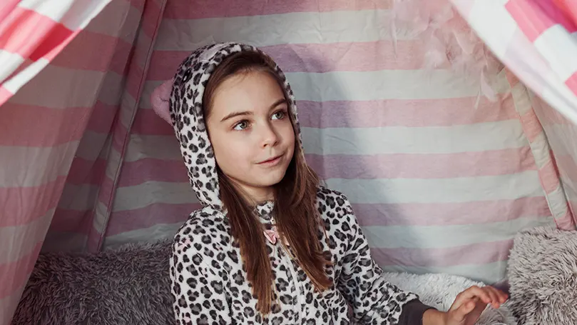 An image of a girl in her pyjamas under a big blanket fort