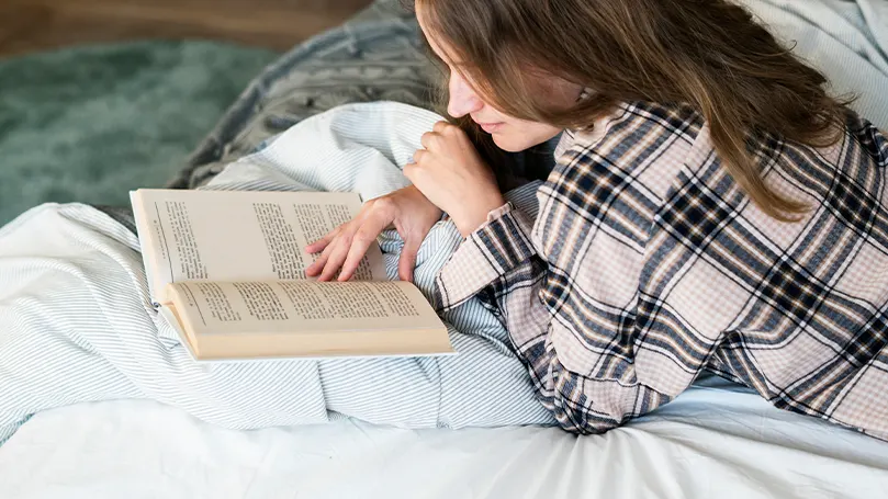 An image of a woman reading a book in bed.