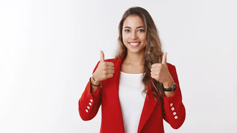 An image of a woman smiling and holding two thumbs up