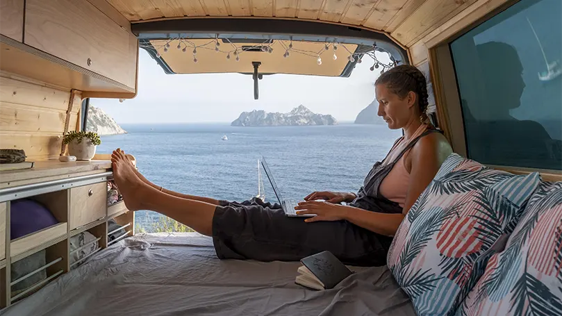 An image of a young woman sitting on a mattress in a camping van