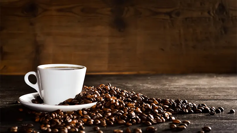 A cup of coffee with coffee beans all around it