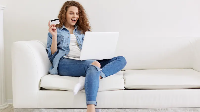 An image of a woman sitting on the couch and buying something online