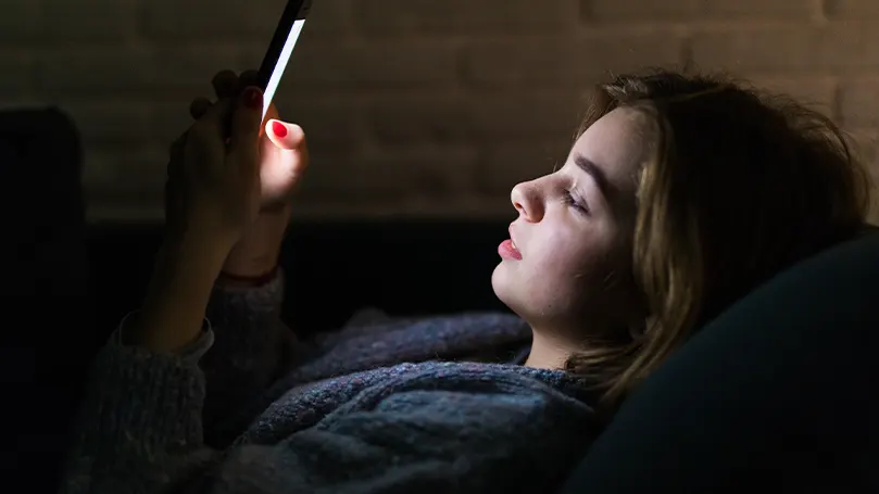 An image of a girl looking at her phone while in bed
