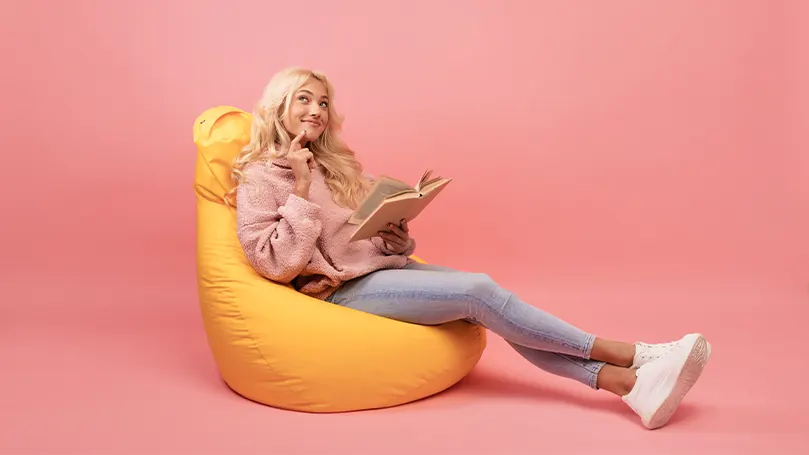 An image of a woman reading in a yellow bean bag chair
