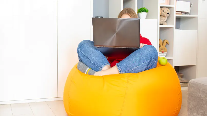 An image of a woman sitting with her legs crossed on a yellow bean bag chair