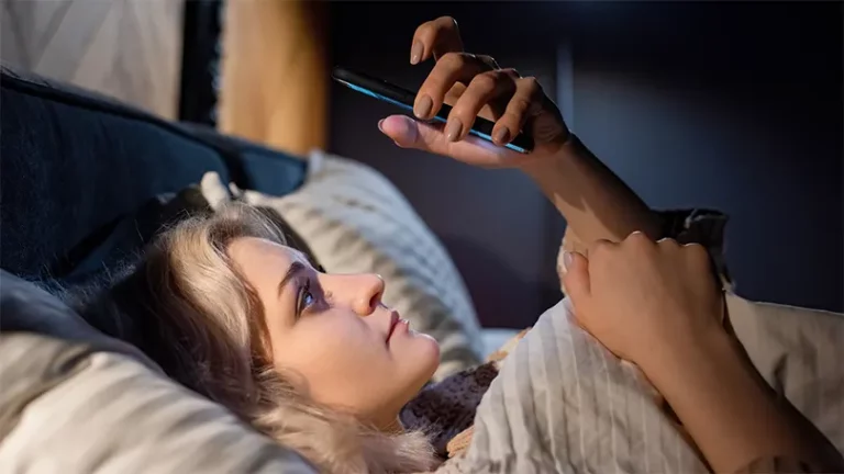 An image of a woman in bed holding a phone