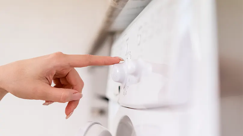 An image of a woman turning on a washing machine