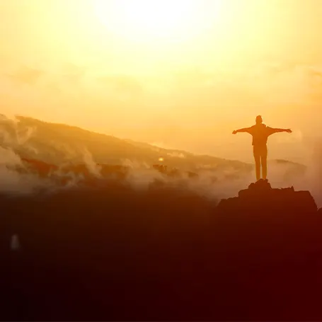 An image of a man atop a mountain with the face beaming in their face