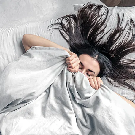 An image of a woman in bed pulling her duvet over her face