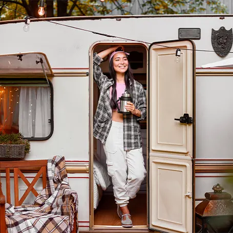 An image of a woman coming out of her camping van with a cup of coffee in hand