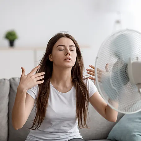 An image of a woman cooling down by pointing a fan at herself