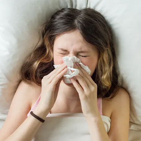 An image of a woman holding a tissue to her nose after her bedding triggered her allergies