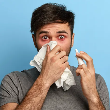An image of a man with allergies holding a tissue to his nose
