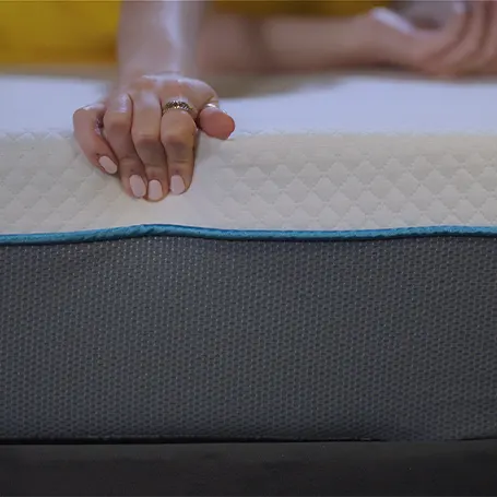Hand pressing on the edge of the mattress.