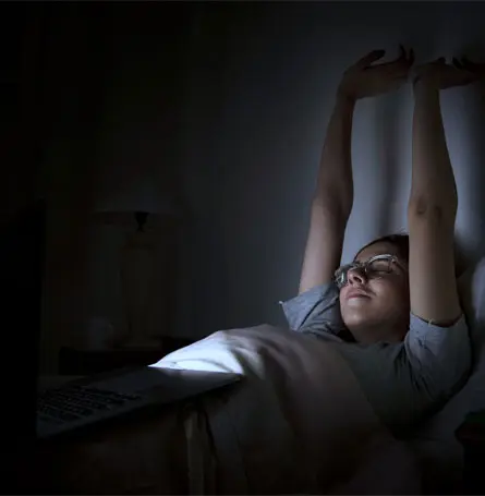 An image of a woman in bed with artificial light lighting up her face