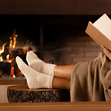 An image of a person using an electric blanket and reading a book in front of a fireplace