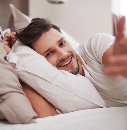 An image of a person in their bed in the morning smiling