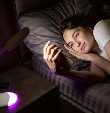 An image of a woman watching at her phone in bed with light hitting her face
