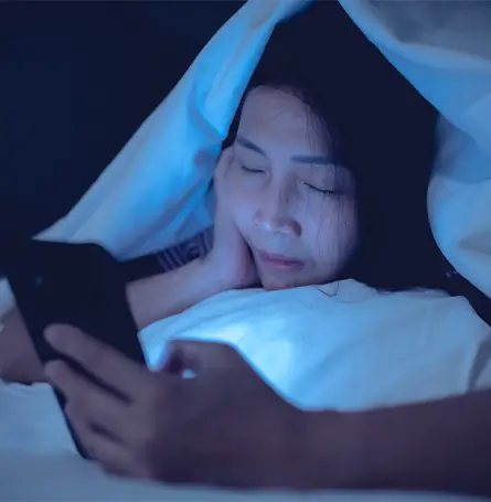 An image of a woman in bed looking at her phone